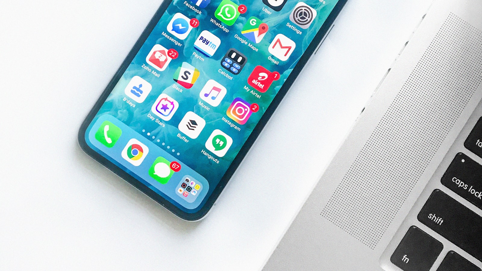 A smartphone home screen full of app icons resting beside a laptop keyboard