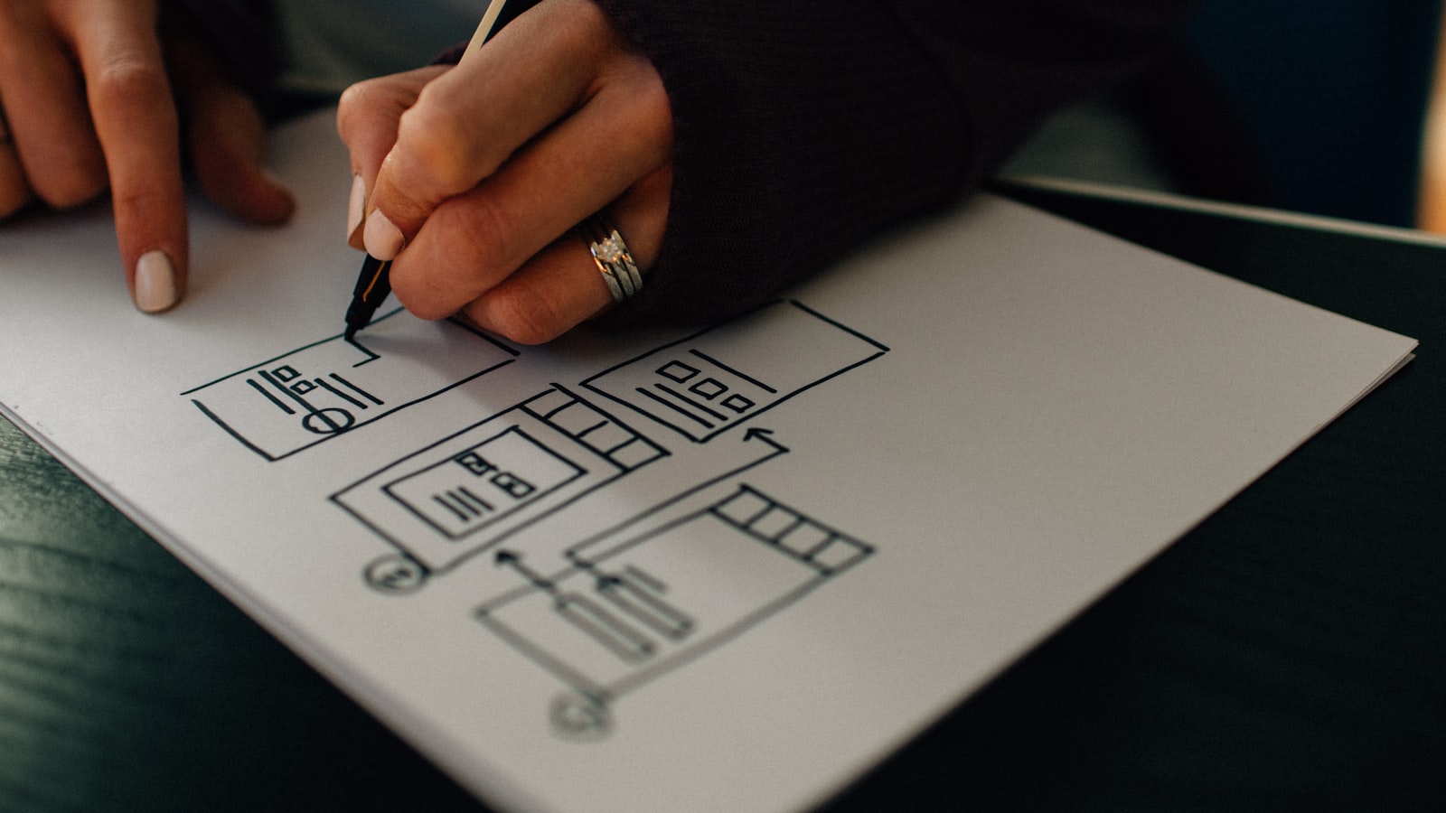 A hand sketching interface wireframes on paper with a pencil
