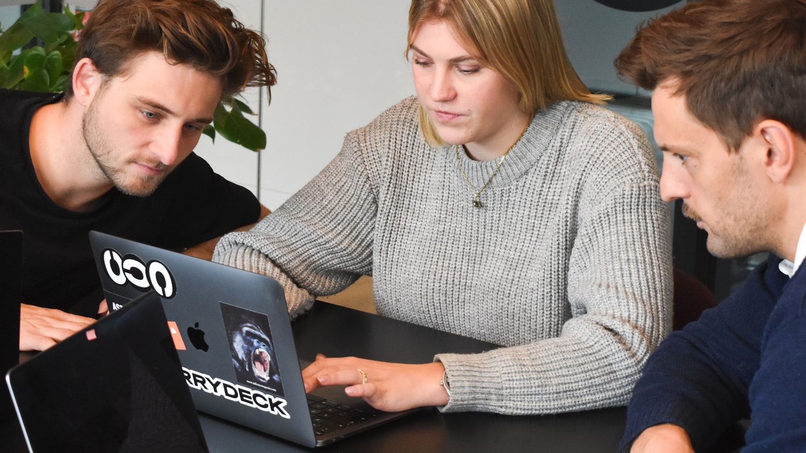 Three people looking closely at a laptop screen together at a desk