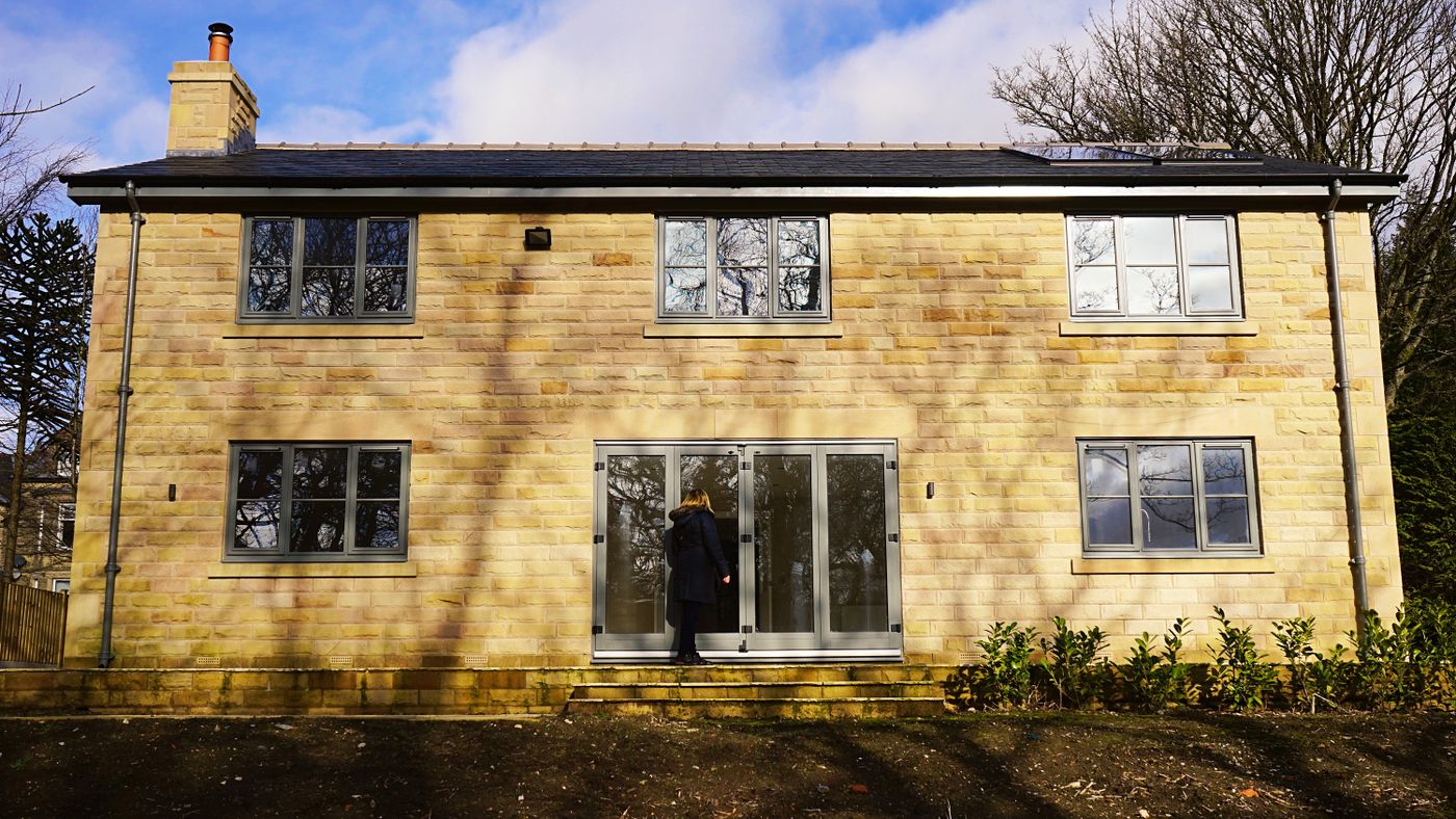 A newly built stone house with grey window frames and bifold doors.