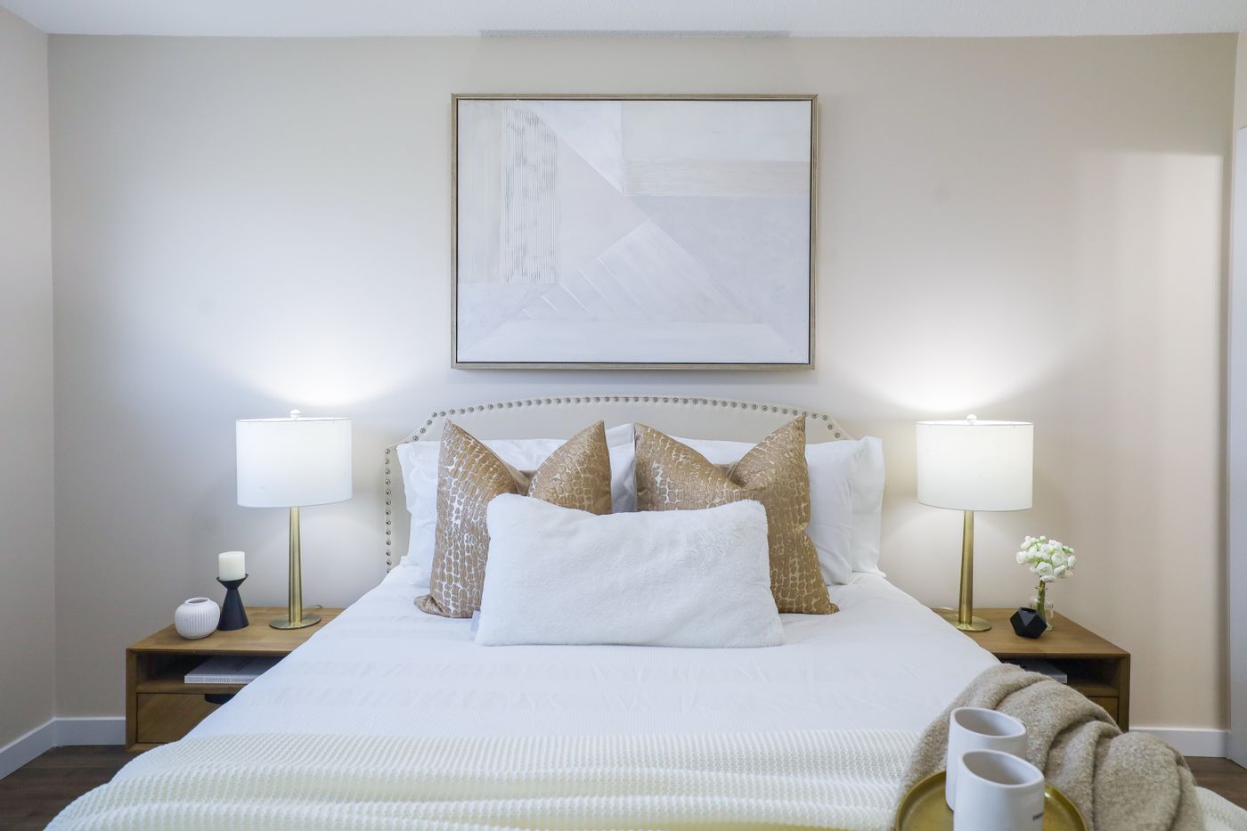 A staged bedroom in neutral tones with layered bedding and matching lamps.