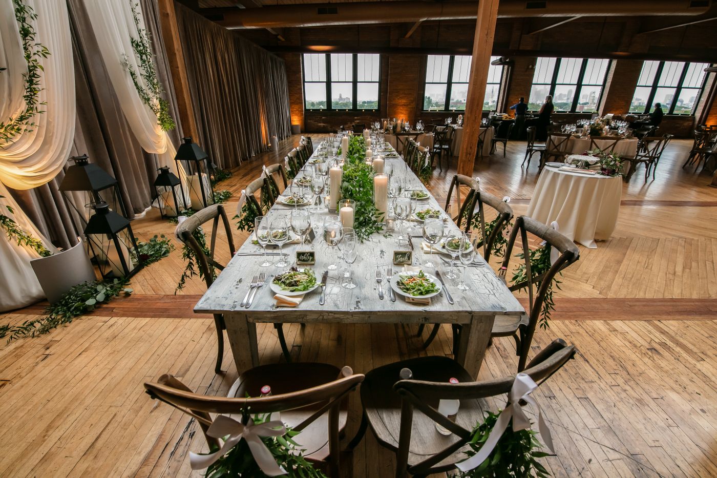 A long banqueting table dressed with candles and greenery in a brick loft.