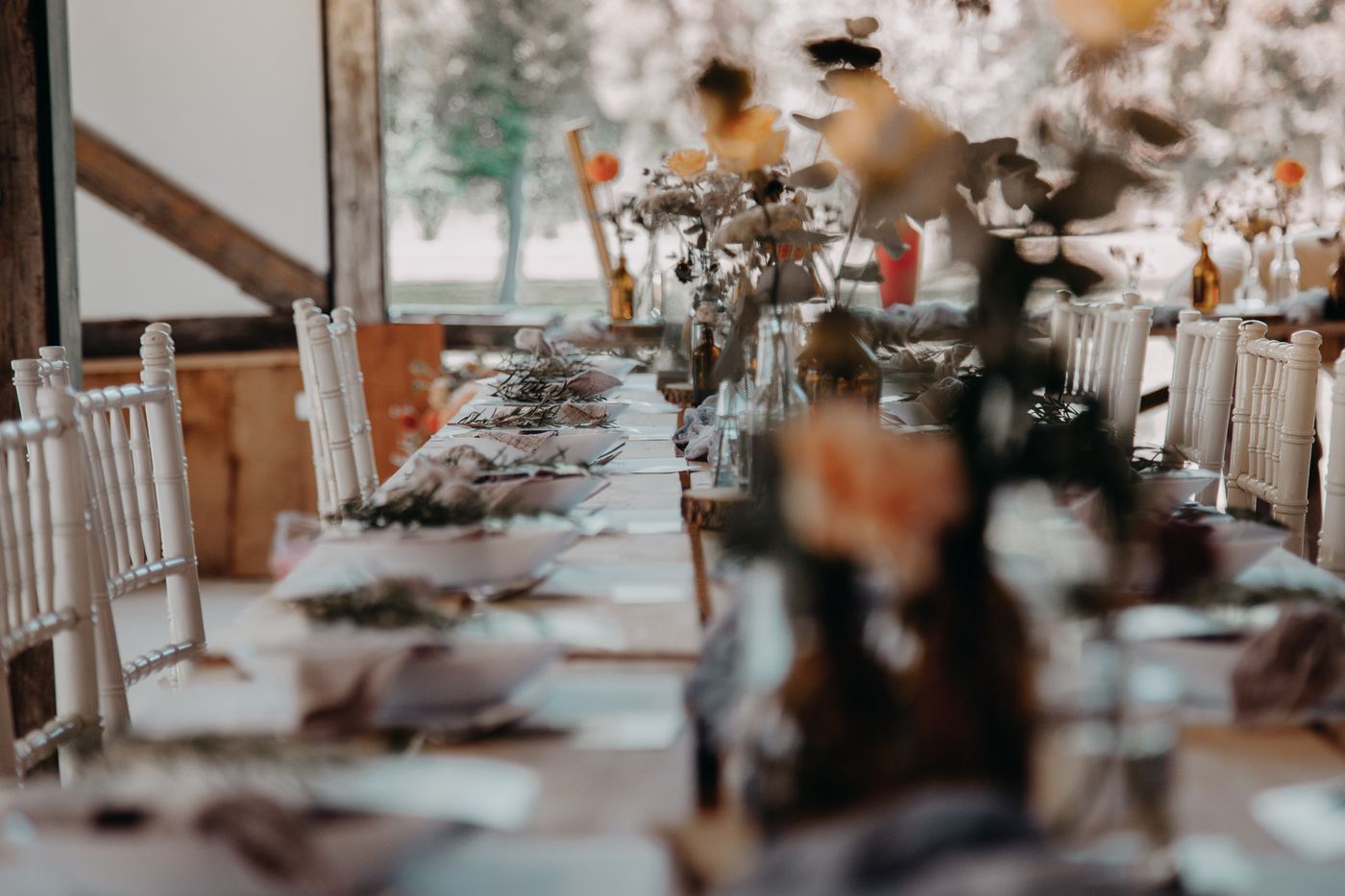 A long table in a timber barn dressed with dried florals and mixed glassware.